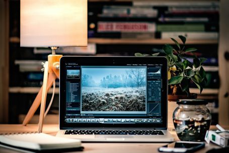IT-Fernwartung und Online-Support ohne Anfahrt Laptop mit geöffnetem Bildbearbeitungsprogramm, daneben eine Lampe und Bücher im Hintergrund.